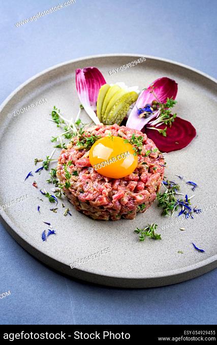 Gourmet tartar raw from beef fillet with yellow of the egg and baguette as closeup on modern design dish