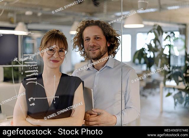 Portrait of confident businessman and businesswoman behind glass pane in office