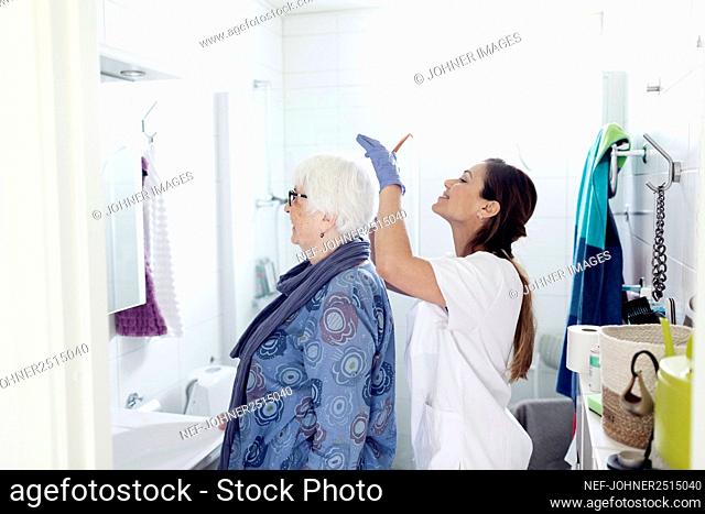 Nurse combing woman's hair in bathroom