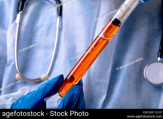 Close up of health worker inserting syringe into test tube with chemical