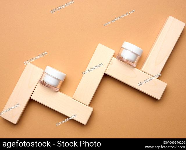 empty white glass jar for cosmetics on a brown background and wooden blocks. Packaging for cream, gel, serum, advertising and product promotion