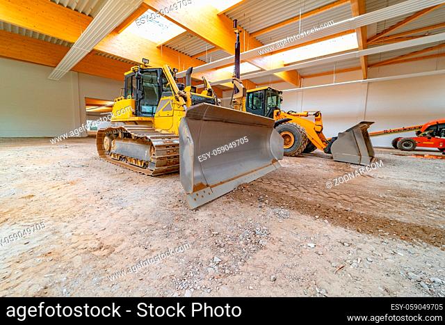 Inside a large factory hall are two large construction machines