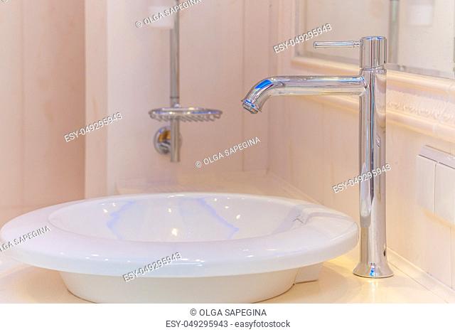 Close up of modern faucet and ceramic sink in bathroom
