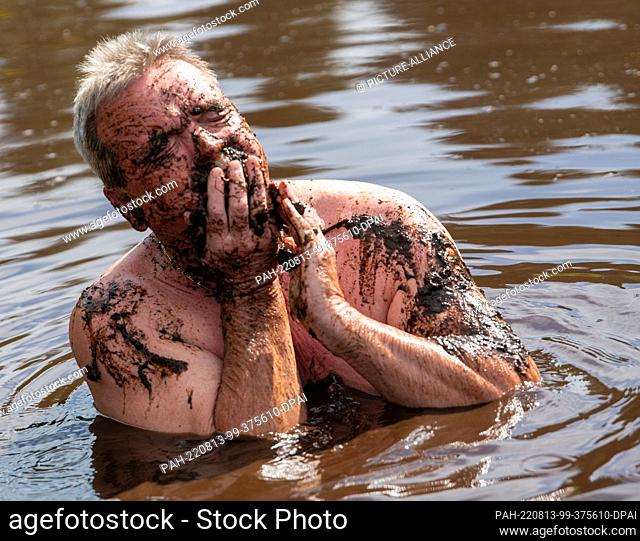 13 August 2022, Bavaria, Buchenberg: Achim Wurster bathes in a mud pond and rubs himself with mud. This way, a wellness effect is added to the refreshment
