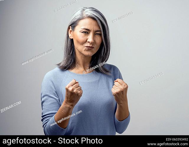 Happy Mature Asian Female Model Smiles Happily. She Celebrates Victory and Holds Fists in Satisfaction. Hand Photo in Studio on White Background