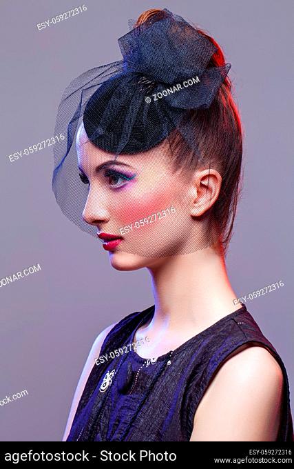 Beautiful young woman in small black veil hat cap with hairdo and bright purple tone make-up. Doll style. Beauty shot on grey background. Copy space