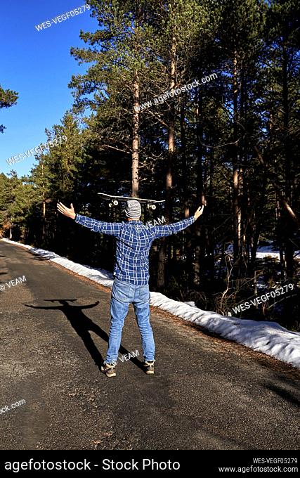 Man standing with arms outstretched balancing skateboard on head