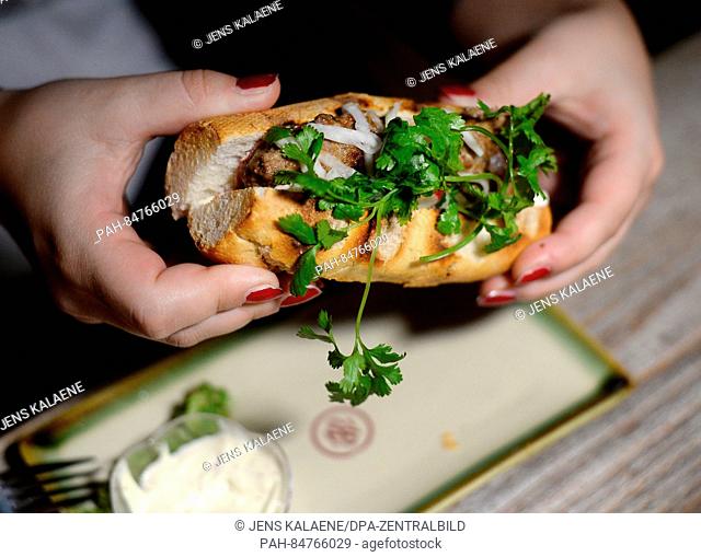 A woman holds the street food sandwhich 'Banh Mi' with a Berlin meatball, radishes, kohlrabi sweet-sour and liver sausage along with Spree forest cucumber...