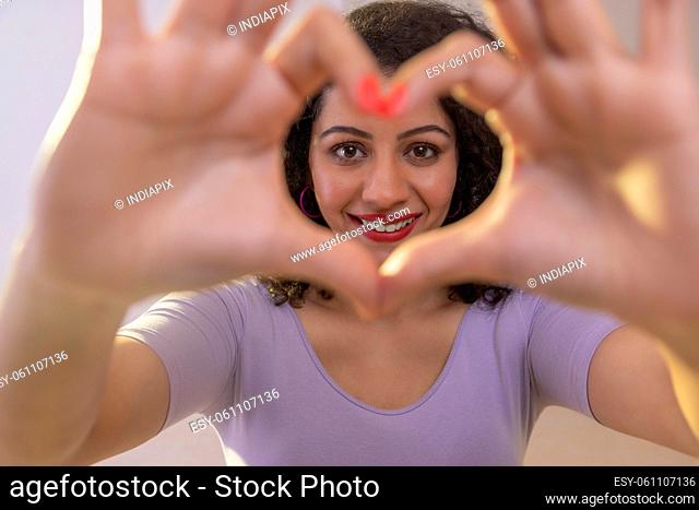 Adult woman forming heart shape with her fingers and looking at camera through it
