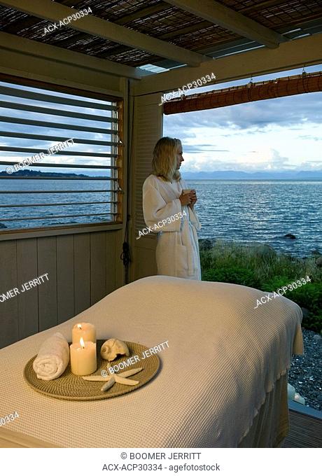 A young woman gazes out ot the Ocean in front of a beach front massage hut. Courtenay, The Comox Valley, Vancouver Island, British Columbia, Canada