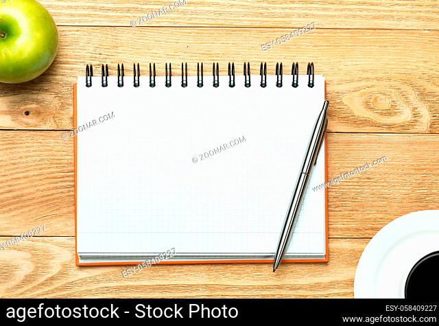 White blank notepad with cup of coffee and green apple on wooden table