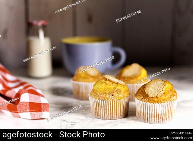 four delicious cupcakes, milk bottle, blue ceramic cup and napkin on marble table on wooden background