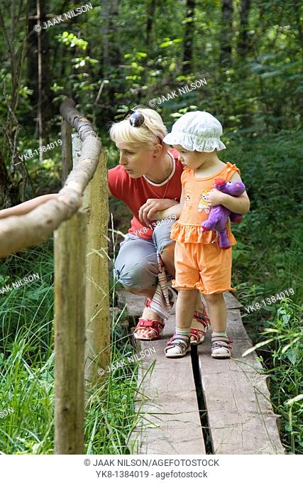 Mother with Kid Girl Standing on Wooden Boardwalk with Fence in Forest