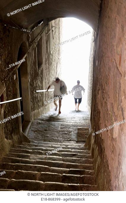 Italy, Linguria, Porto Venere.  Men ascending stairs through an arched tunnel from seaside up to the main street