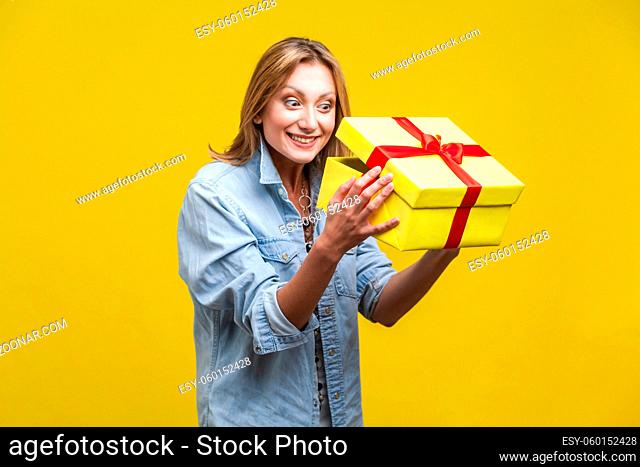 Long awaited present. Portrait of curious woman in denim shirt looking inside gift box, checking what's inside, unboxing with satisfied happy expression