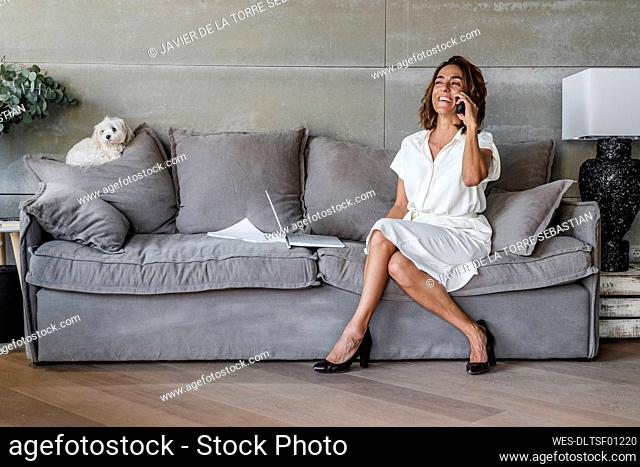 Smiling woman talking on mobile phone while sitting on sofa at office