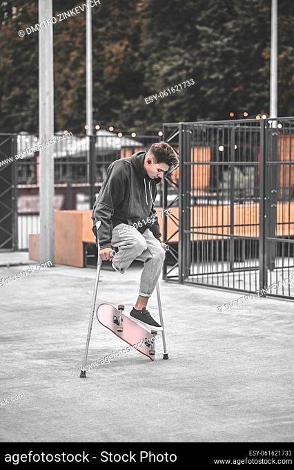 Inclusiveness. Disabled guy on crutches flipping skateboard in air with his foot on skateboarding site