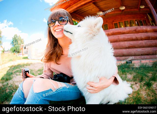 young stylish hipster woman girl playing white kid-skin dog in country side, village wood house, cool outfit, romantic mood, having fun, ripped jeans