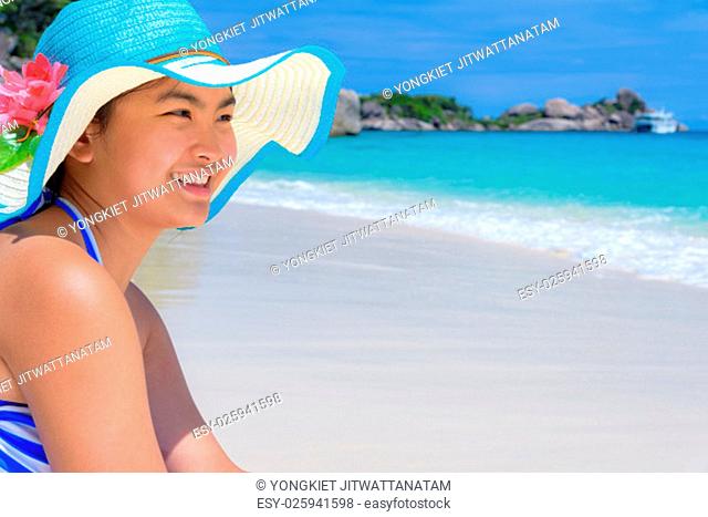 Girl in a blue swimwear sitting a happy on the beach with the sea as background during summer at Koh Miang Island, Mu Ko Similan National Park