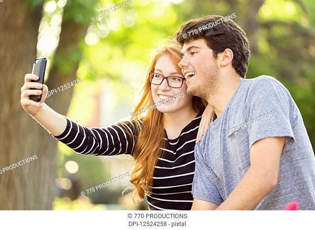 A young man and young woman taking a self-portrait on a smart phone; Edmonton, Alberta, Canada