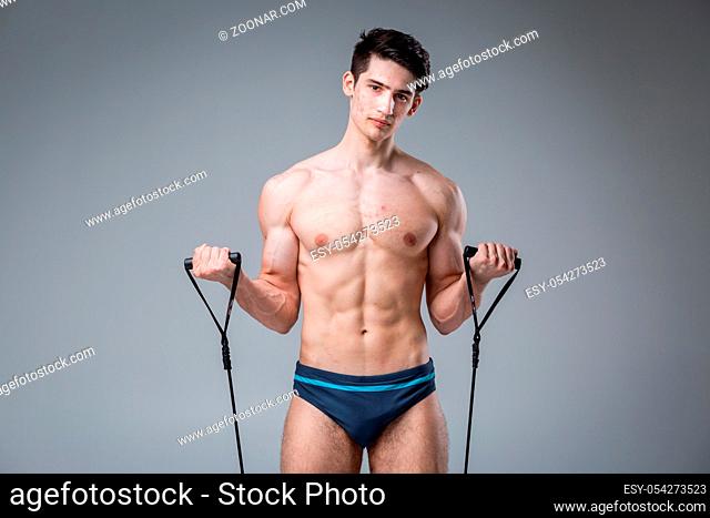 Studio portrait young Caucasian man on gray background posing. theme of puberty, problem skin, teen acne. Caucasian athlete uses banding for fitness