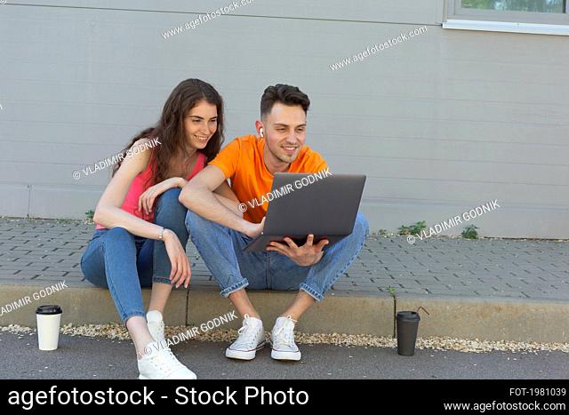 Young couple using laptop on curb