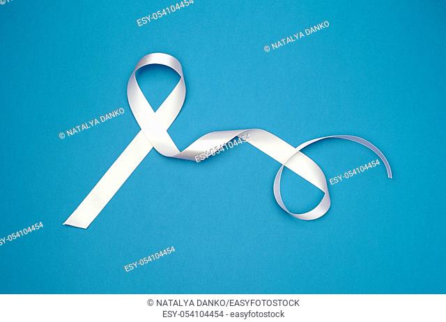 white silk thin ribbon twisted on a blue background, looped tape with long ends, top view