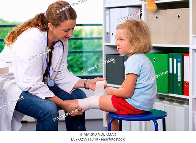 female pediatrician in white lab coat bandaging the leg of a little girl