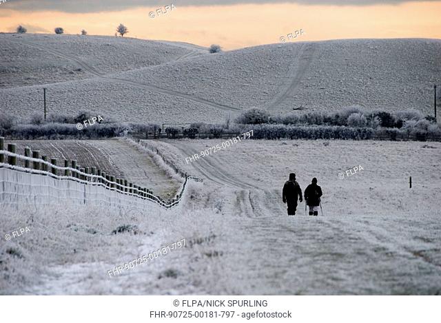 Walkers on frost and snow covered footpath at sunset, Ridgeway Path, near Pitstone Hill, Chilterns, Buckinghamshire, England, december
