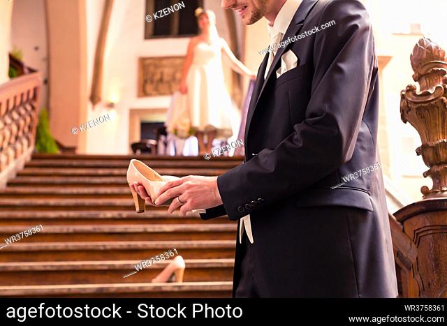Smiling bridegroom holding high heel in his hand standing in front of staircases