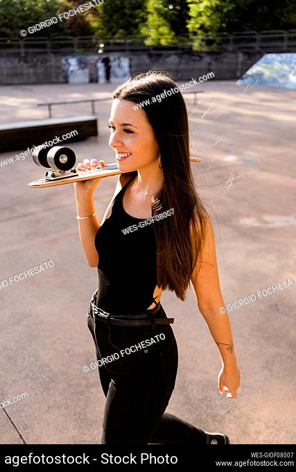Young woman with skateboard on her shoulder at a skatepark