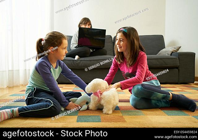 two girls play on the living room carpet with stuffed animals while their mother teleworks on the couch