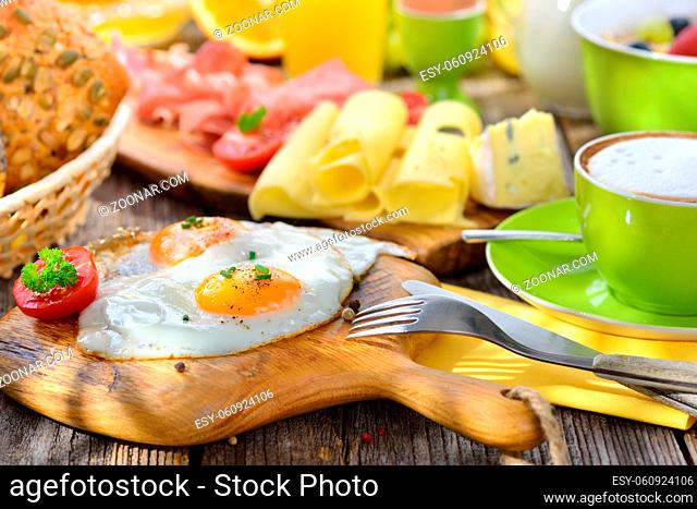 Gedeckter, rustikaler Frühstückstisch im Sonnenlicht mit Spiegeleiern und weiterer reichlicher Auswahl - Outside served breakfast with fried eggs a wide...
