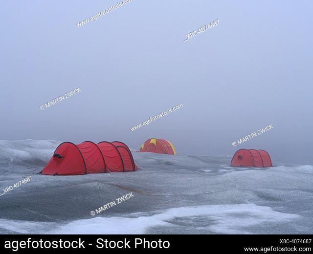 Camp with tents on the ice sheet. The brown sediment on the ice is created by the rapid melting of the ice. Landscape of the Greenland ice sheet near...