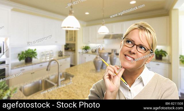 Attractive daydreaming woman with pencil inside beautiful custom kitchen