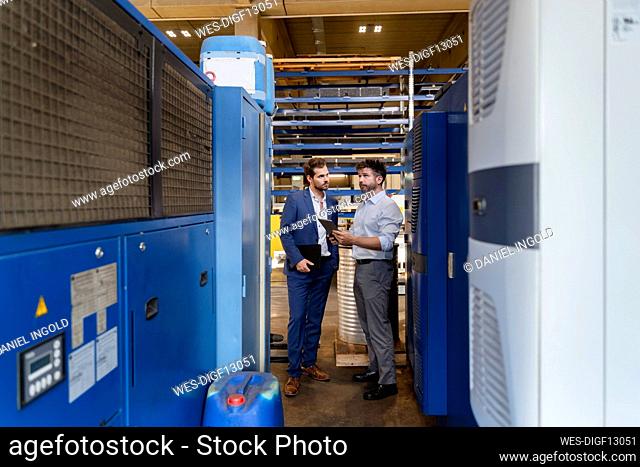 Businessman and colleague with digital tablet examining equipment while standing at factory