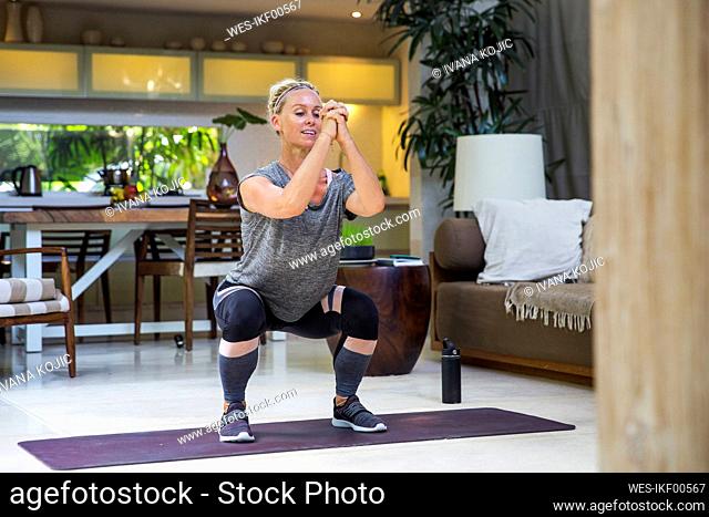 Woman practicing squats on exercise mat at home