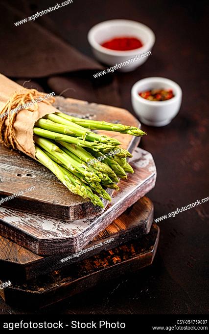 Fresh raw green asparagus on wooden cutting board on gray background