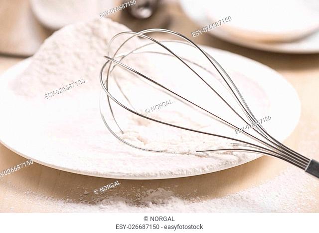 Whisk lying in white wheat flour