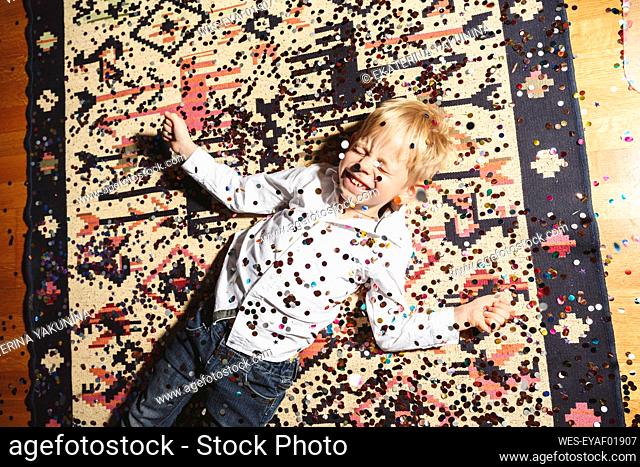 Cheerful boy lying on floor covered with confetti