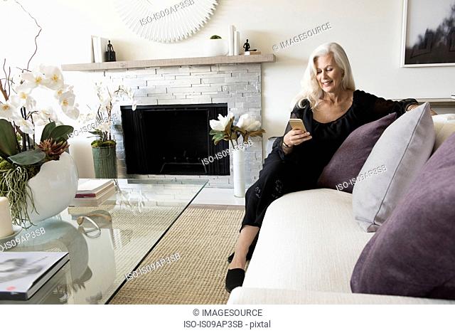 Senior woman sitting on sofa, looking at her phone
