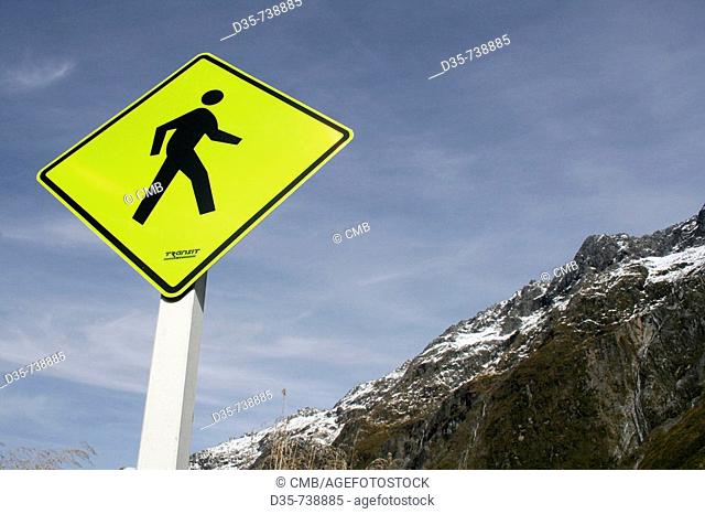 Yellow road sign: pedestrian crossing and mountain range of Milford Sound, Fiordland NP, South Island, New Zealand