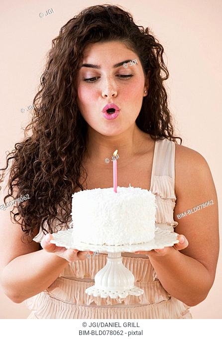 Mixed race woman blowing out candle on birthday cake