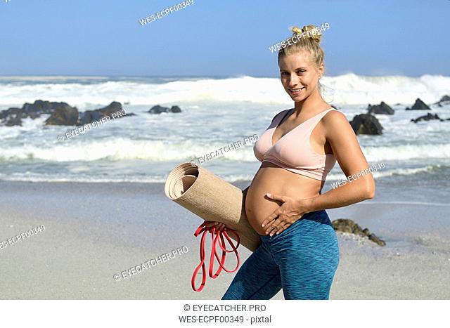Portrait of active pregnant woman holding gym mat on the beach