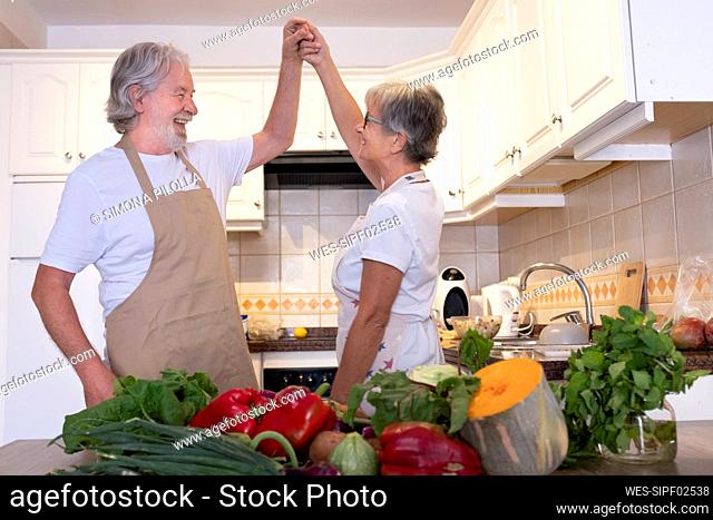 Senior couple holding hands while dancing in kitchen