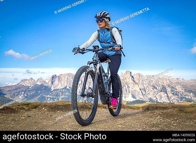 woman cyclist riding an e-bike on tour in the dolomites, pralongia–€  plateau, livinallongo del col di lana, belluno, veneto, italy