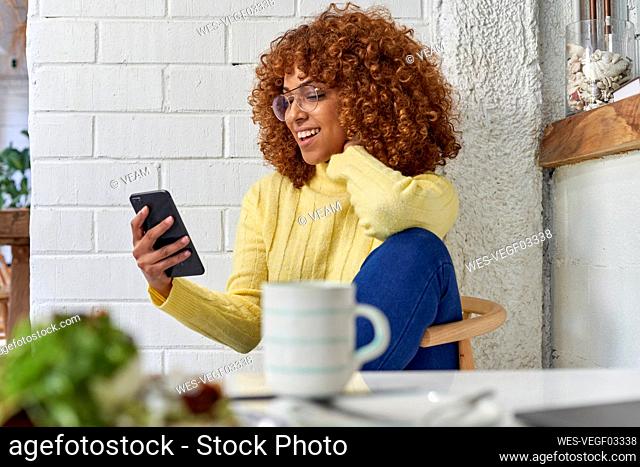 Happy female entrepreneur with coffee cup checking mobile phone in cafe
