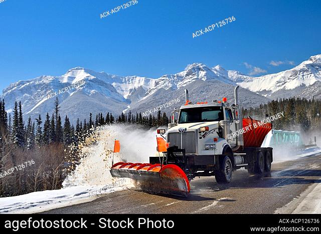 A truck plowing snow on a two lane highway in the rocky mountains near Brule Alberta, Canada