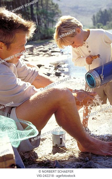 outdoor, close-up, blond 6-year-old boy holds a blue jug pouring water for his father to wash his hands  - GERMANY, 19/09/2004