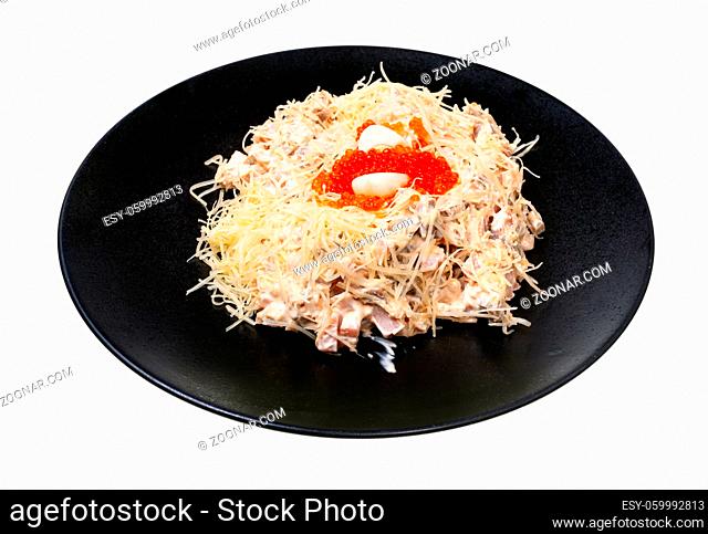 portion of Quail Nest salad from ham, veal and beef tongue, grated cheese, dressed with mayonnaise and decorated by quail egg and salmon caviar on black plate...